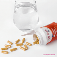 Conceive Plus motility support capsules with a glass of water on a white background
